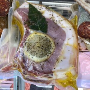Rouelle de porc crue, marinée sous vide avec une rondelle de citron, une feuille de laurier et des herbes aromatiques dans de l'huile.
